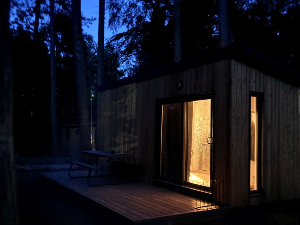 A wooden pod with lights on a deck near trees at Sherwood Pines - Deluxe Pod 2 near Edwinstowe