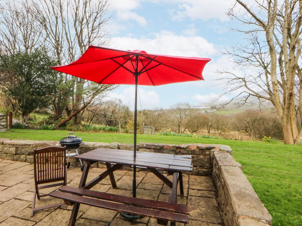 An outdoor seating area with a table, chair, and red parasol at Llwyn Y Brig Isaf in Caernarfon