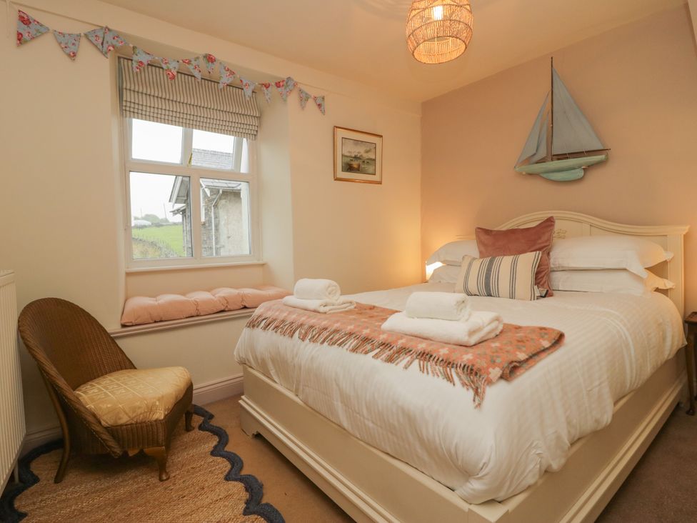 A bedroom with a bed and a wicker chair at Corner Cottage Lowick Green near Ulverston