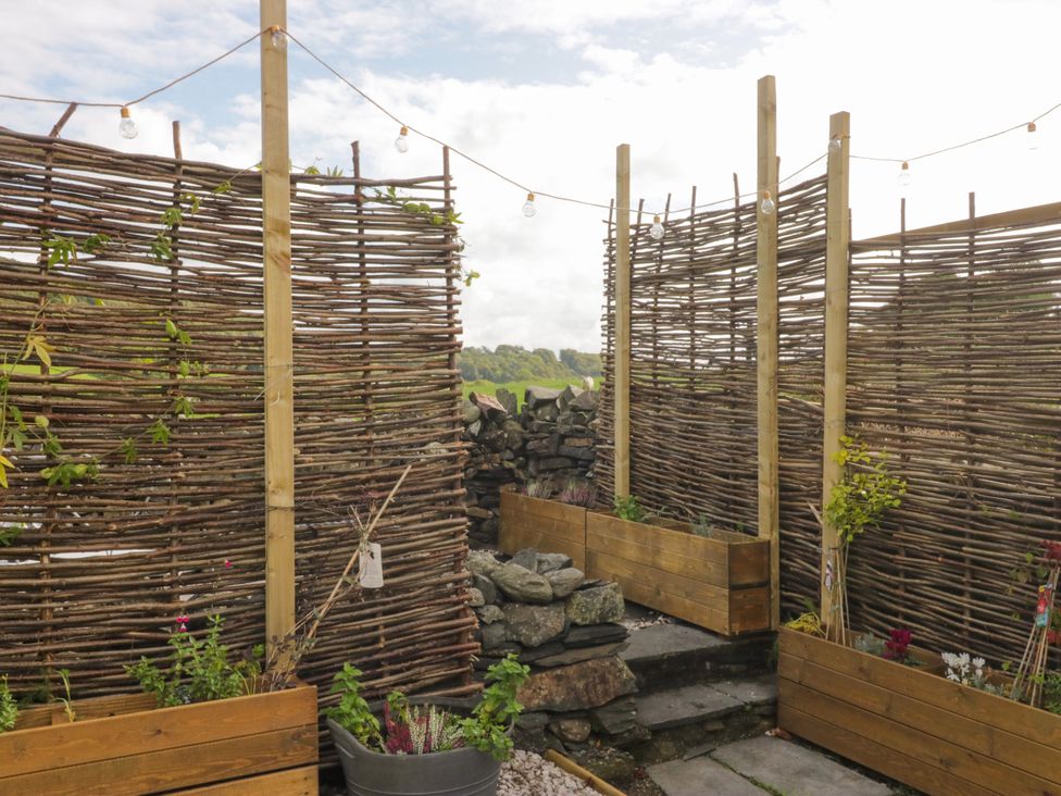 A garden with wooden fencing, plants in pots, and stepping stones at Corner Cottage Lowick Green near Ulverston