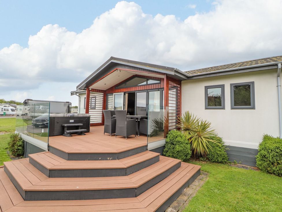 An outdoor deck area with a dining table and chairs at Honeysuckle Lodge in Towyn