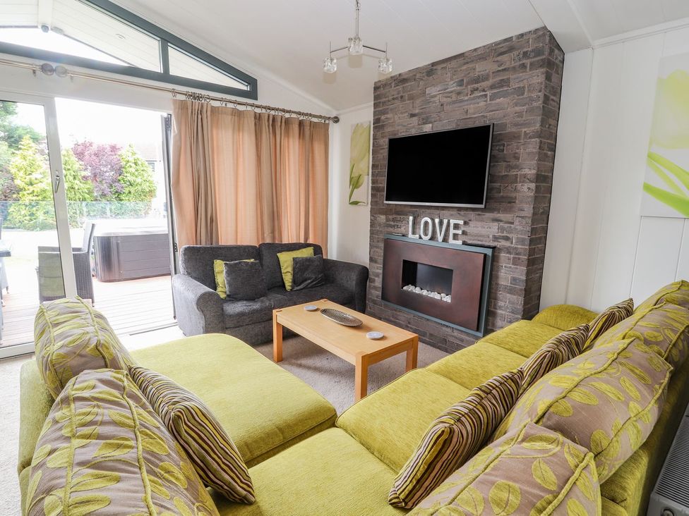 A living room with a television and sofa at Honeysuckle Lodge in Towyn