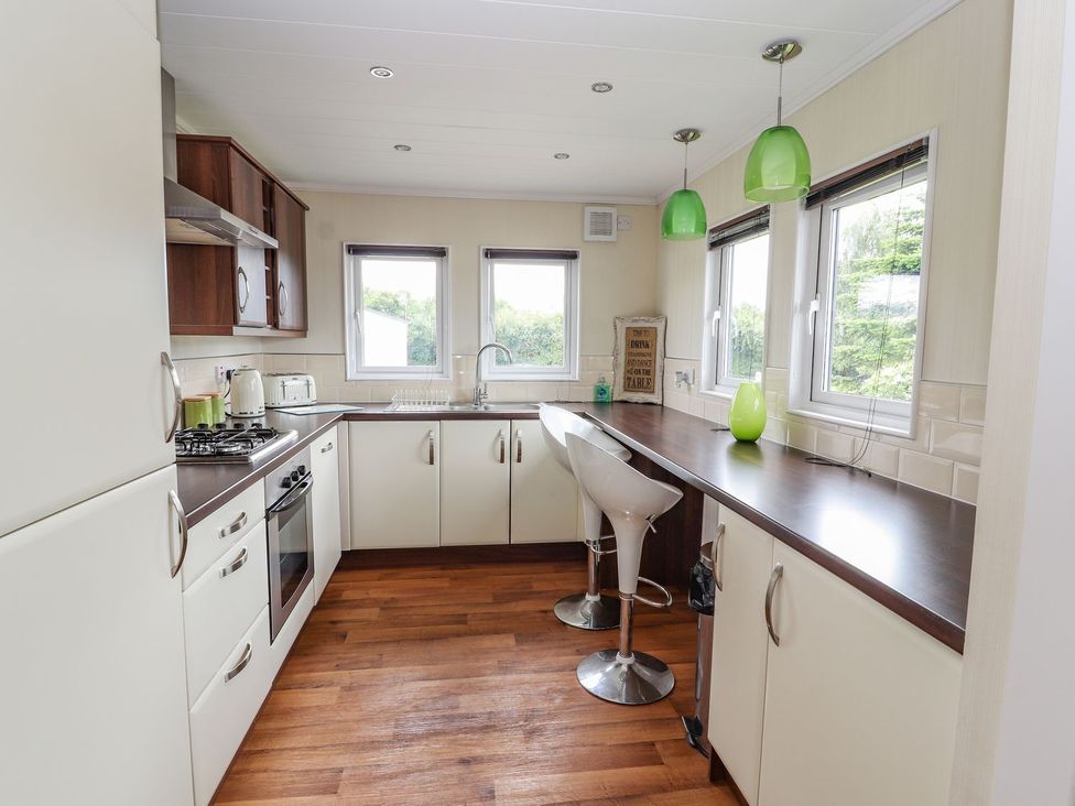 A kitchen with cabinets, countertop, and stools at Honeysuckle Lodge in Towyn