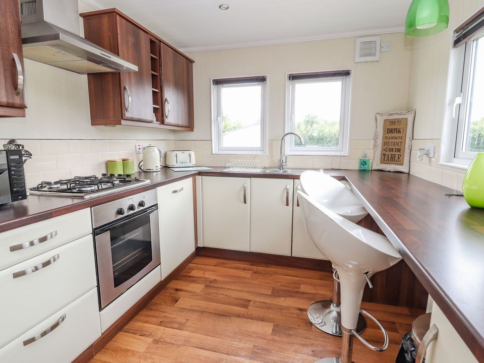 A kitchen with a gas cooker and bar stools at Honeysuckle Lodge in Towyn