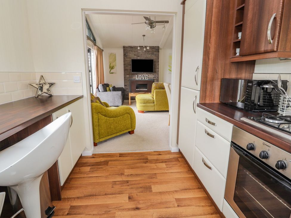 A kitchen with an open view to the living room at Honeysuckle Lodge in Towyn