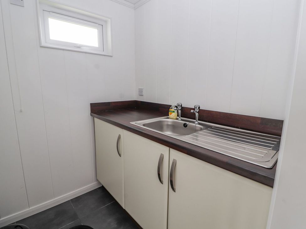 A laundry room with a sink and cupboards at Honeysuckle Lodge in Towyn