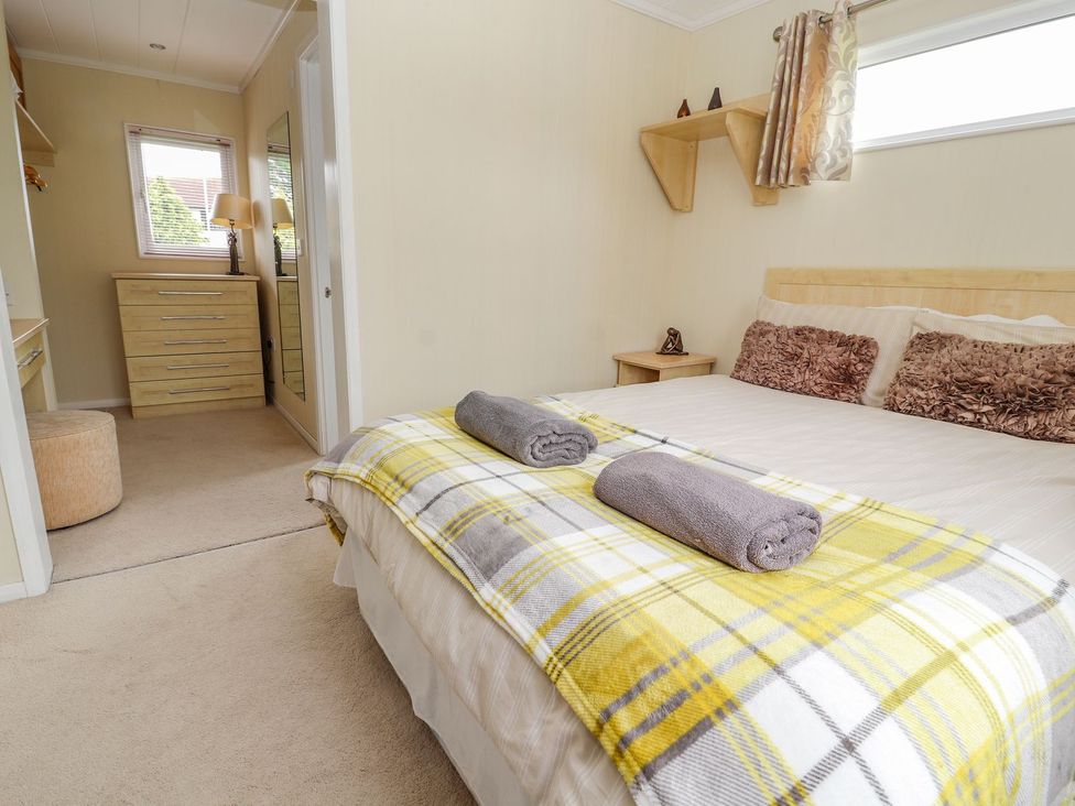 A bedroom with a bed and dresser at Honeysuckle Lodge in Towyn