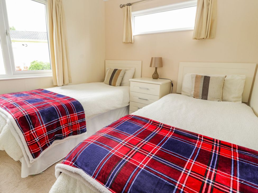 A bedroom with two beds and a nightstand at Honeysuckle Lodge Towyn