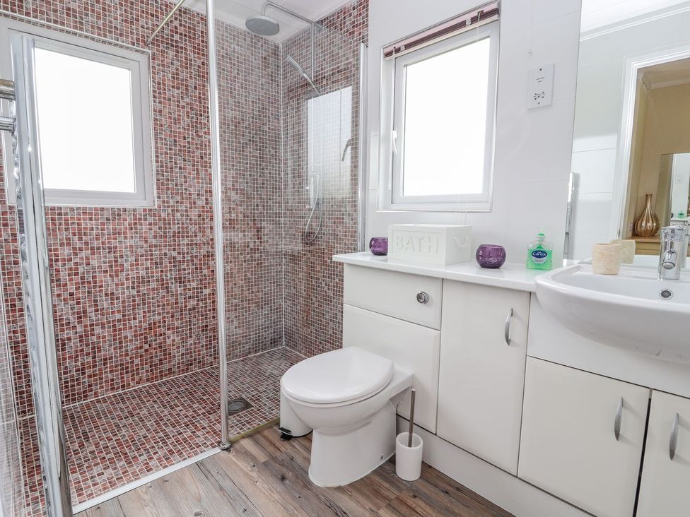 A bathroom with a shower, toilet, and sink at Honeysuckle Lodge in Towyn