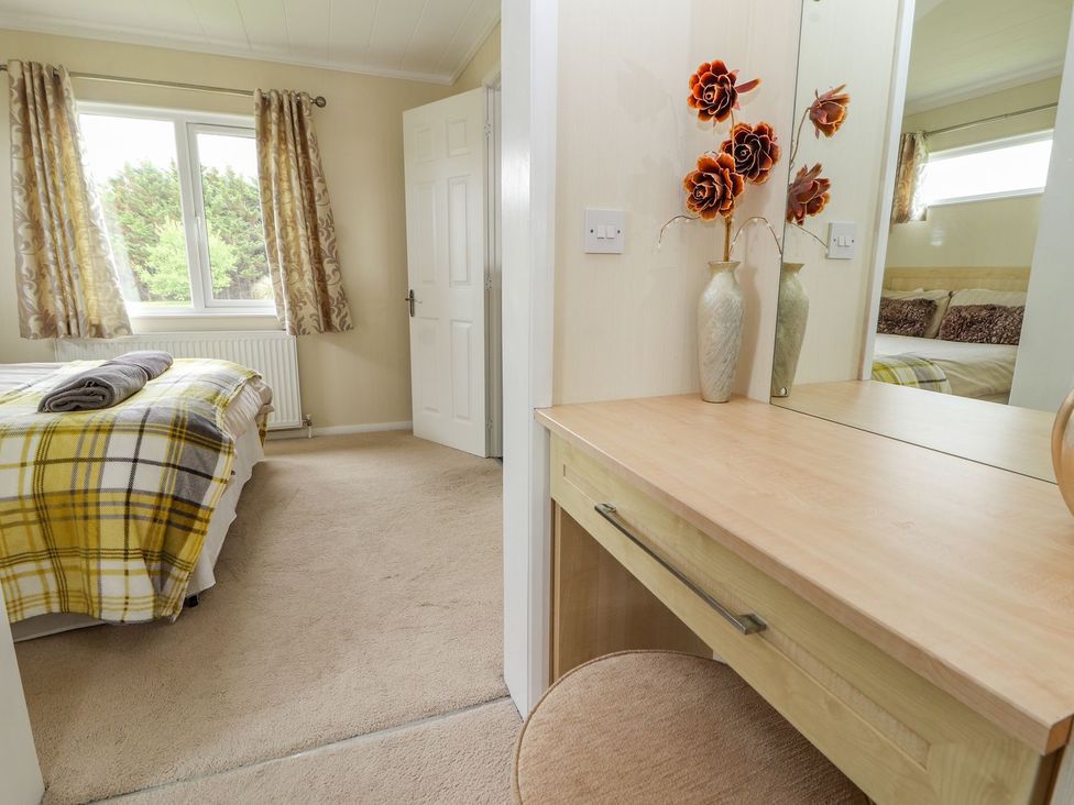 A bedroom with a bed and vanity at Honeysuckle Lodge in Towyn
