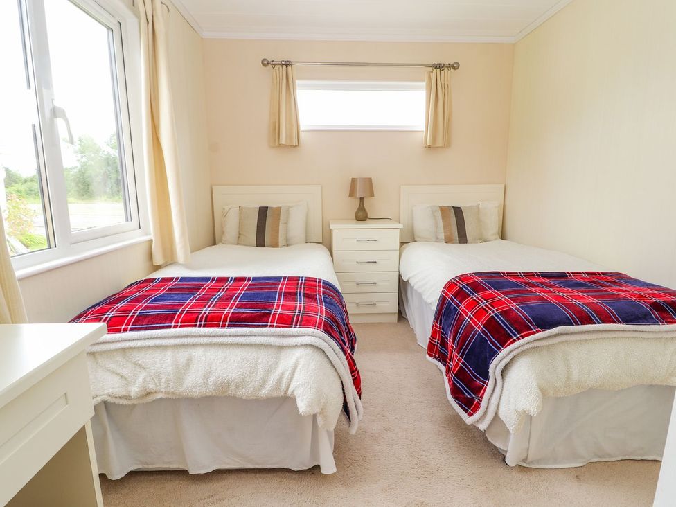 A bedroom with two single beds and a bedside table at Honeysuckle Lodge in Towyn