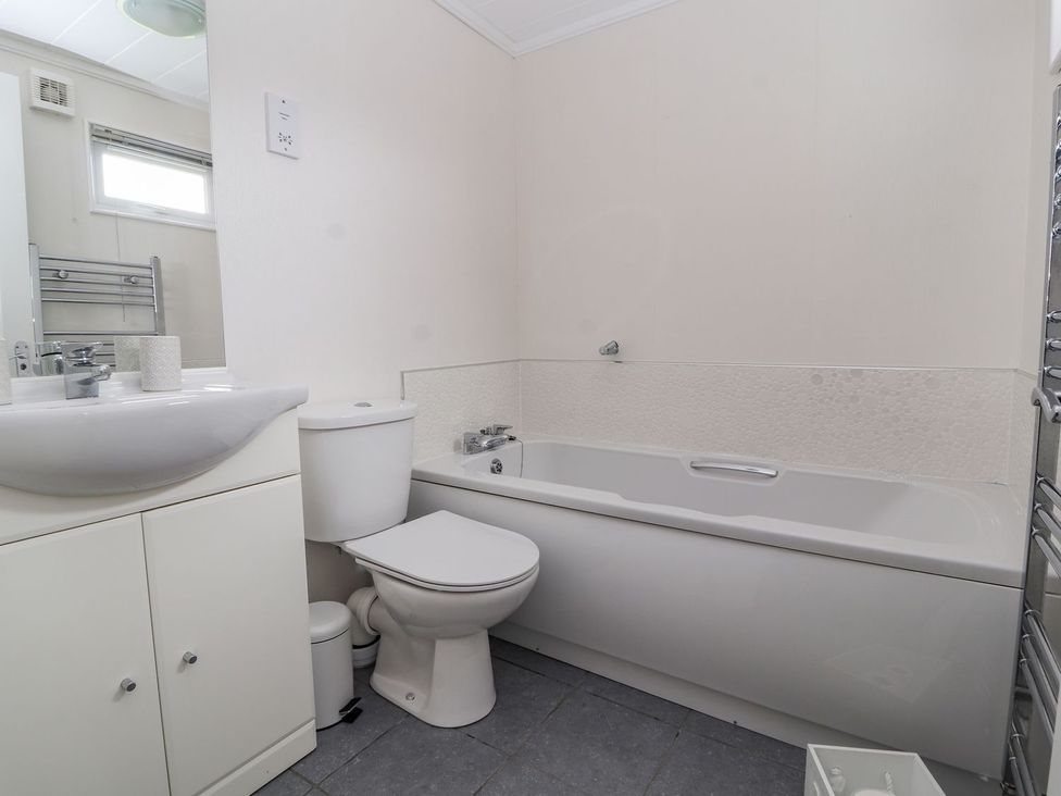 A bathroom with a bath tub, toilet, and sink at Honeysuckle Lodge in Towyn
