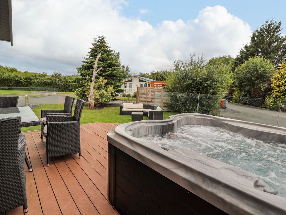 An outdoor area with a hot tub and seating at Honeysuckle Lodge in Towyn