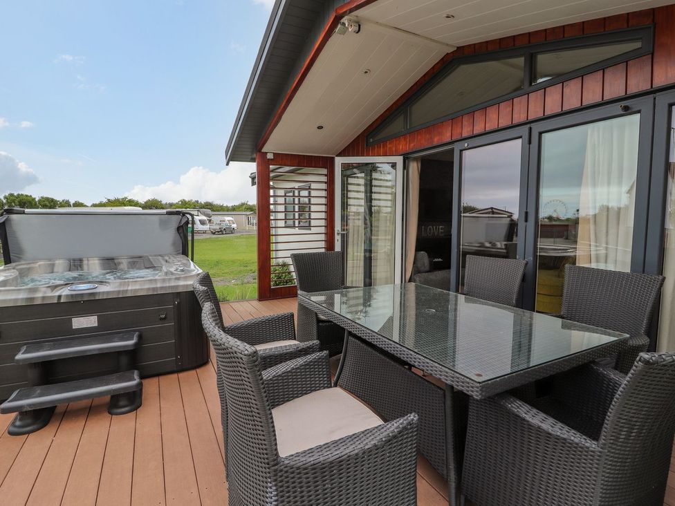 An outdoor area with a hot tub and dining table at Honeysuckle Lodge in Towyn