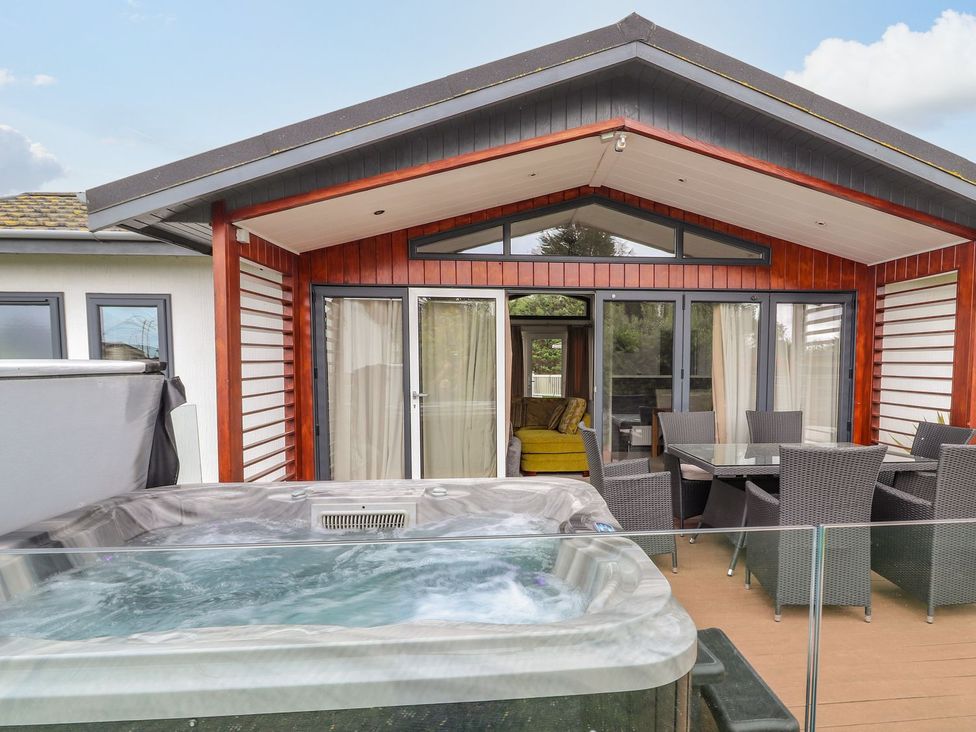 An outdoor patio with a hot tub and dining area at Honeysuckle Lodge in Towyn
