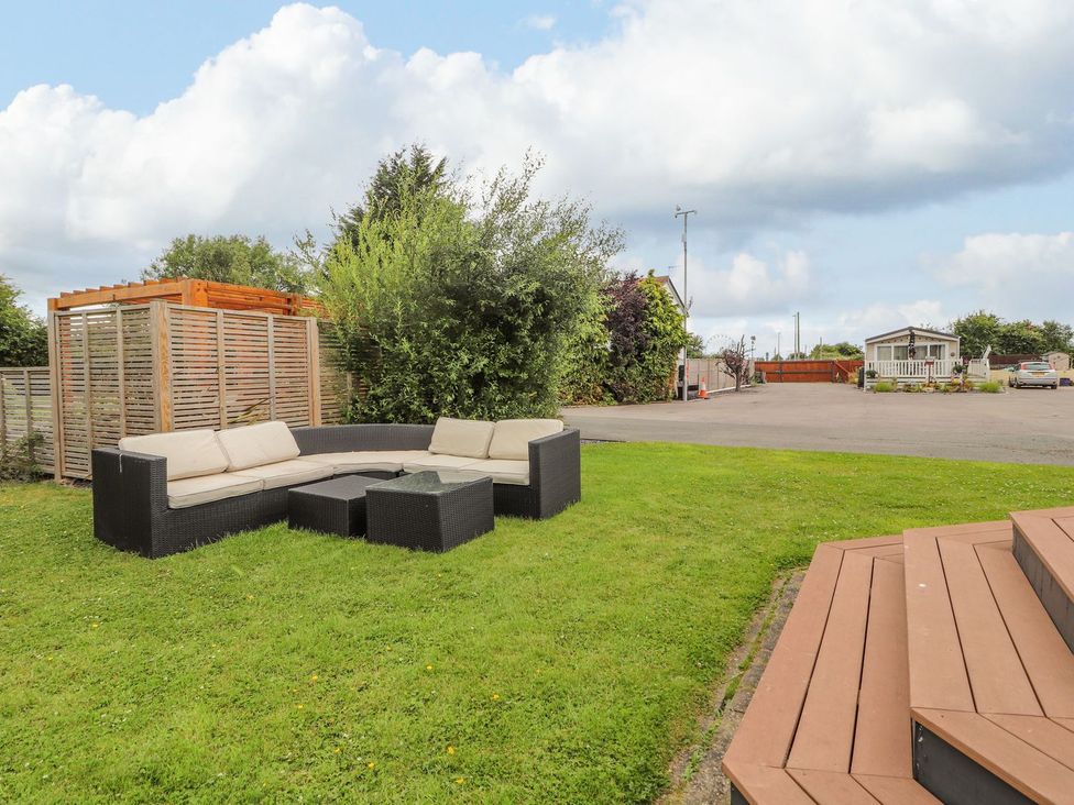 A garden with a sofa and coffee table at Honeysuckle Lodge in Towyn
