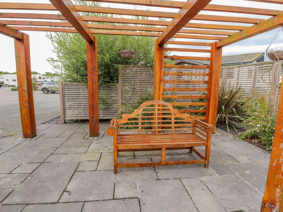 An outdoor area with a wooden bench under a pergola at Honeysuckle Lodge Towyn