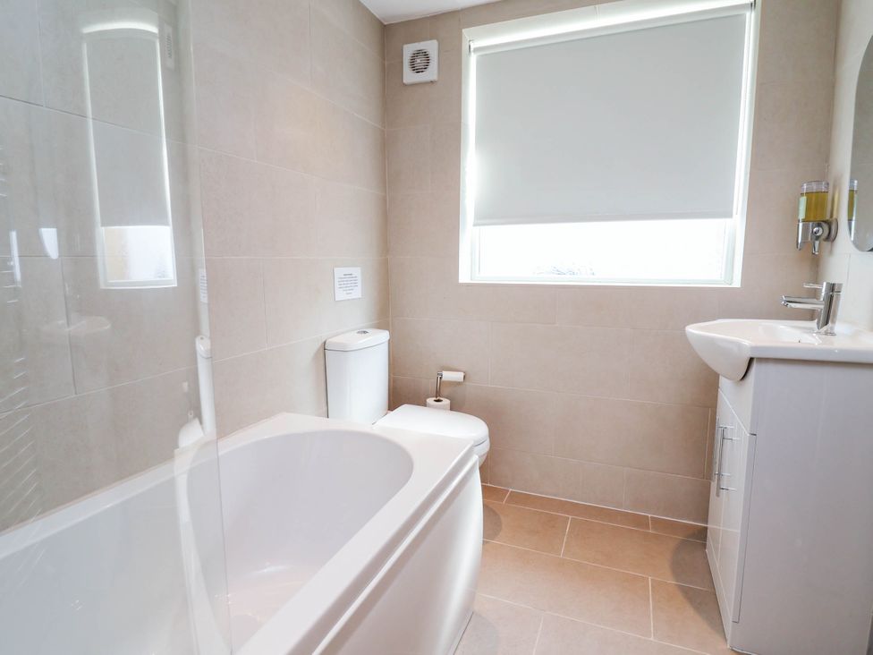 A bathroom with a bath tub, toilet, sink, and window at Brightside in Hoylake