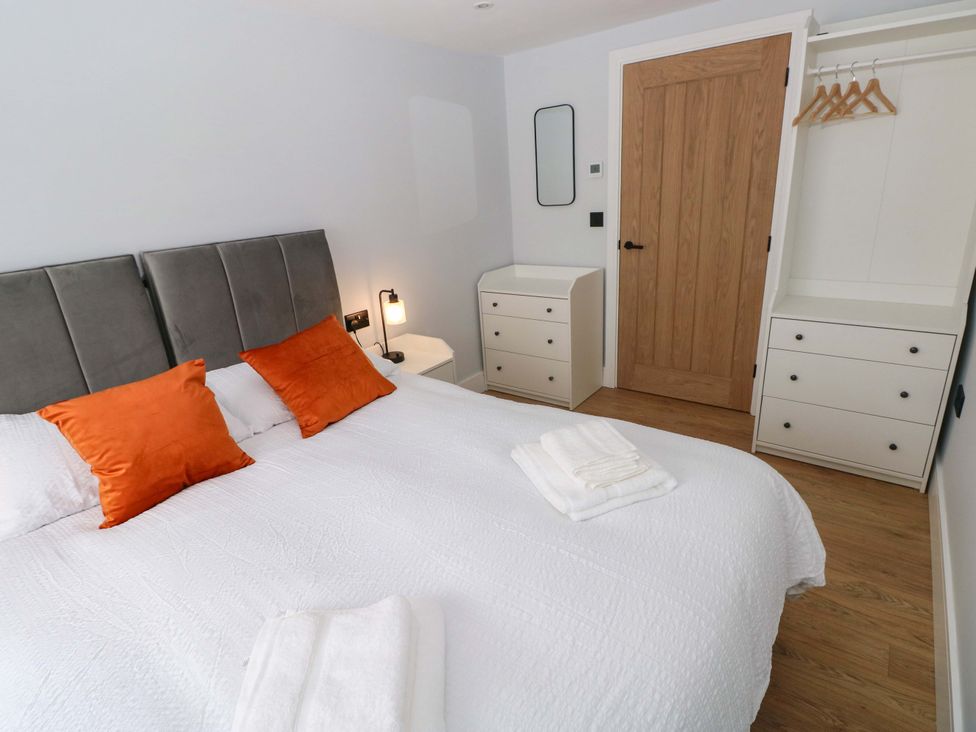 A bedroom with a bed, bedside lamp, dressing table and wardrobe at Y Bwthyn in Burry Port
