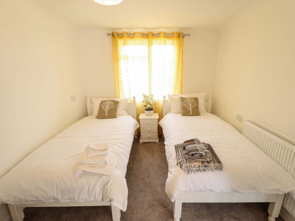 A bedroom with two beds and a bedside table at Four Seasons in Humberston, Lincolnshire