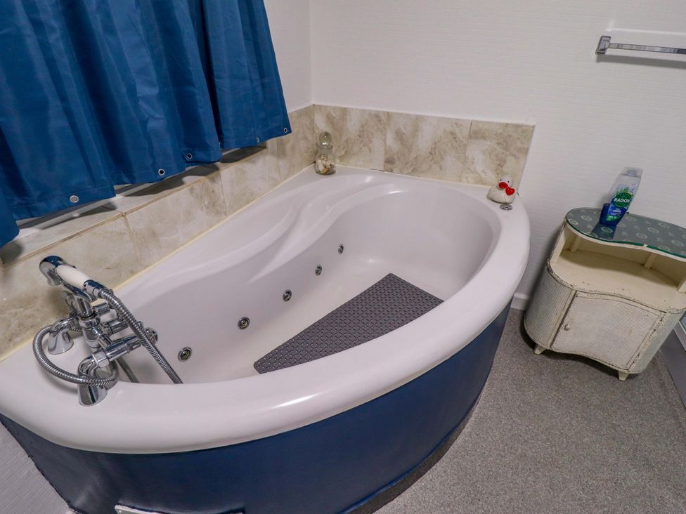 A bathtub with a shower curtain and a side table at Four Seasons in Humberston, Lincolnshire