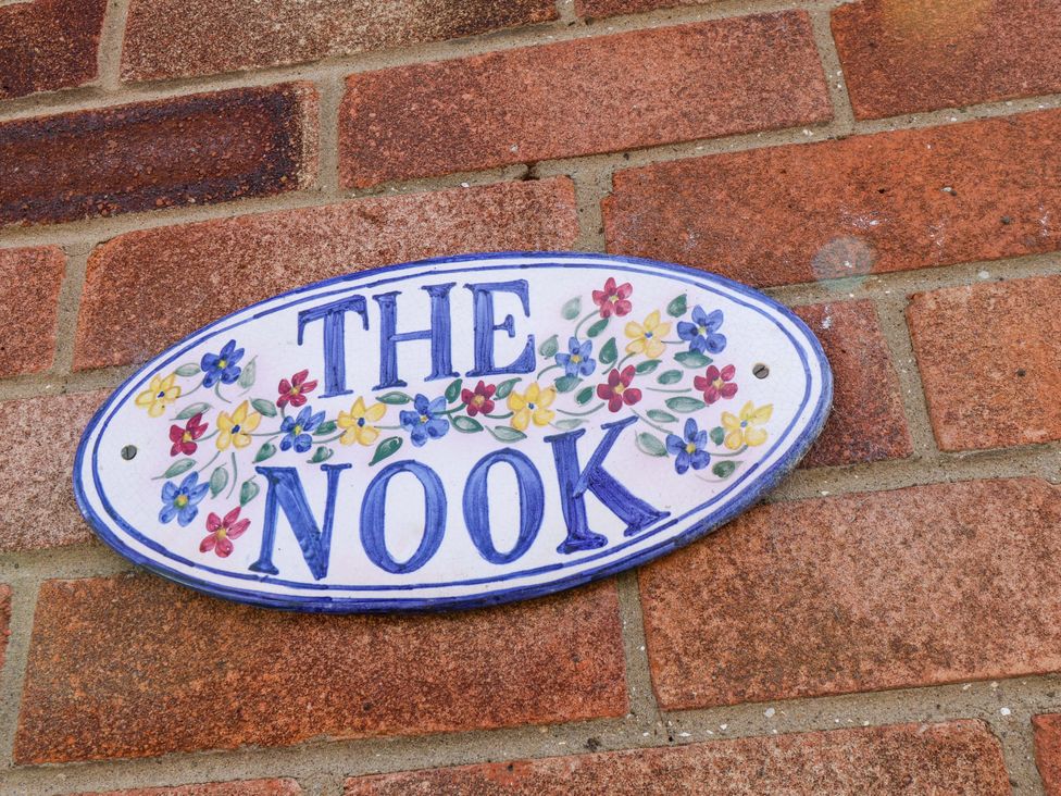 A sign reading THE NOOK with floral decoration on a wall at The Nook in Robin Hood’s Bay
