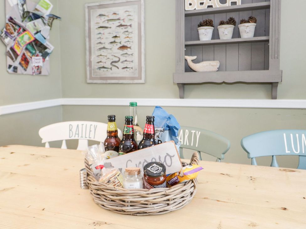 A dining room with a basket of snacks and bottles on a table at 2 Old Coastguard House in Beaumaris