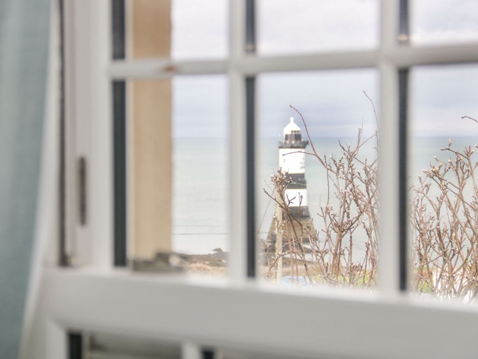 A view of a lighthouse through a window at 2 Old Coastguard House Beaumaris