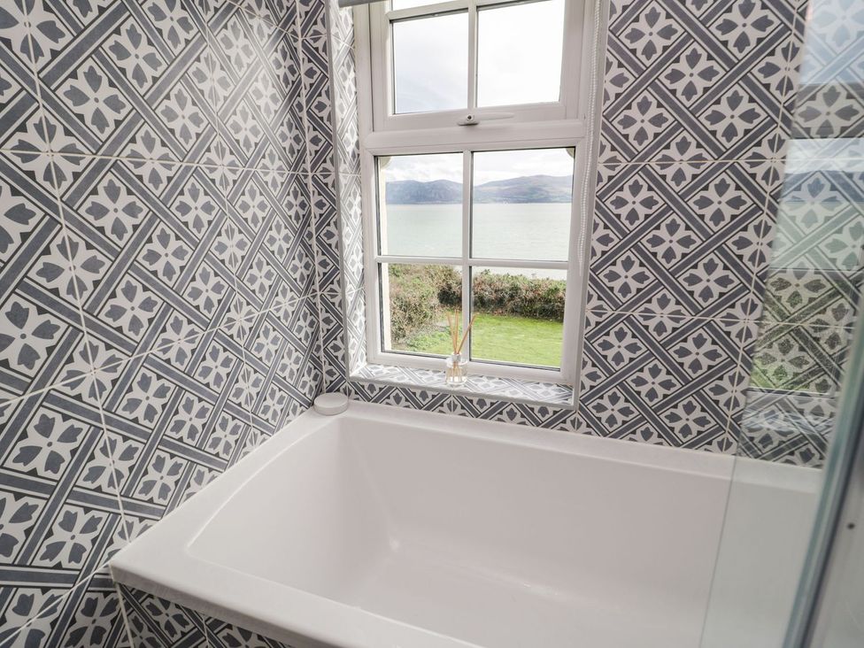 A bathroom with a bathtub and window overlooking the water at 2 Old Coastguard House Beaumaris
