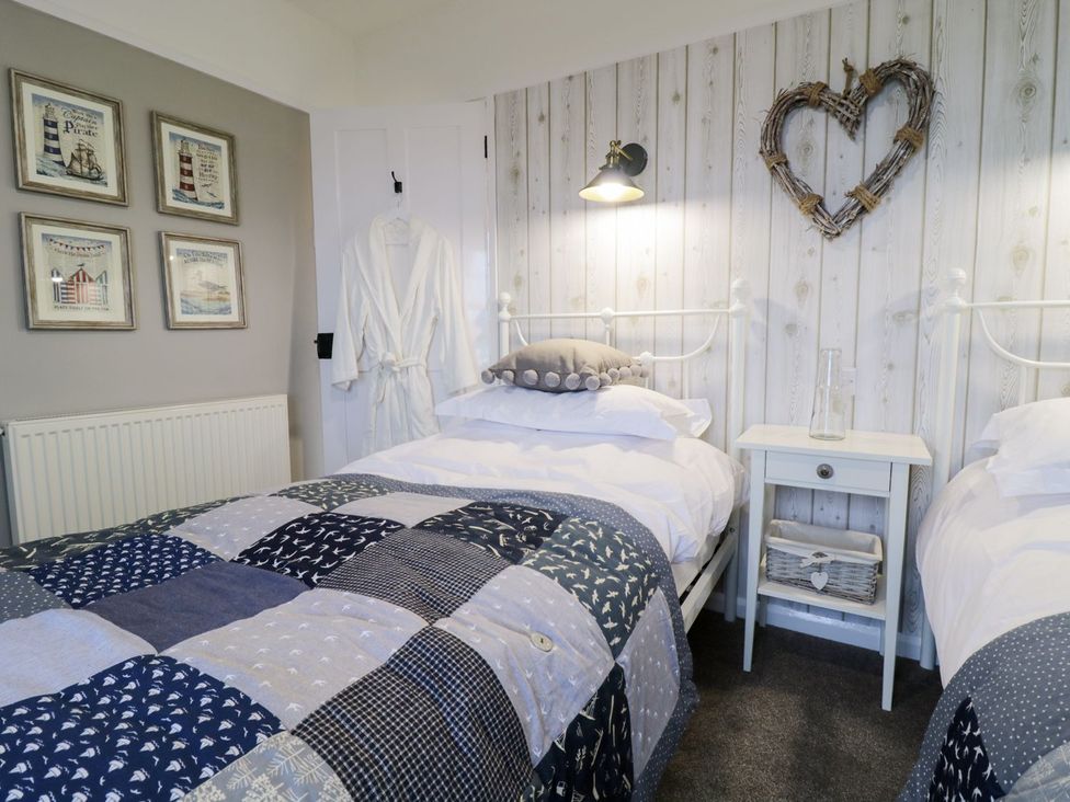 A bedroom with two beds and framed pictures at 2 Old Coastguard House Beaumaris