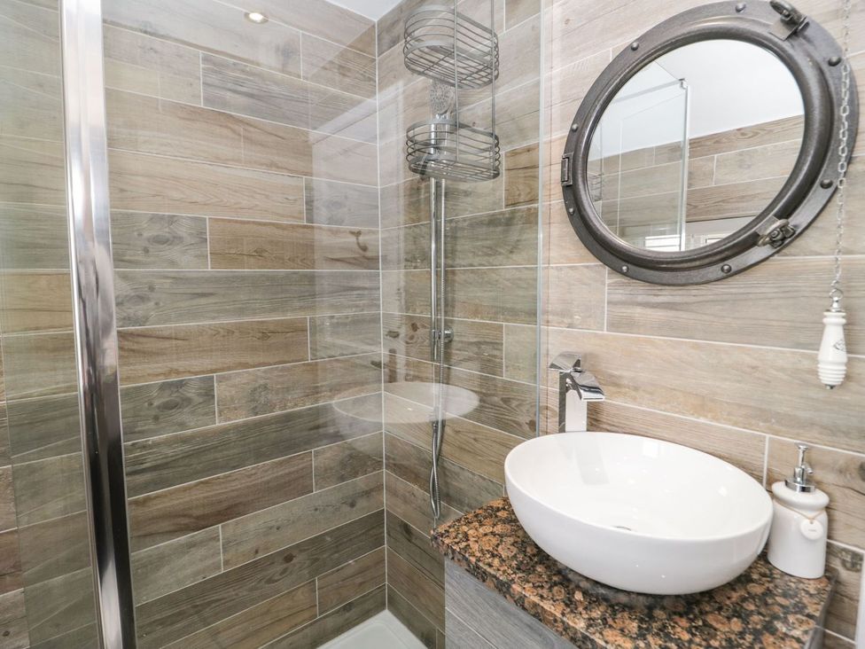A shower stall with a circular mirror and wash basin at 2 Old Coastguard House Beaumaris