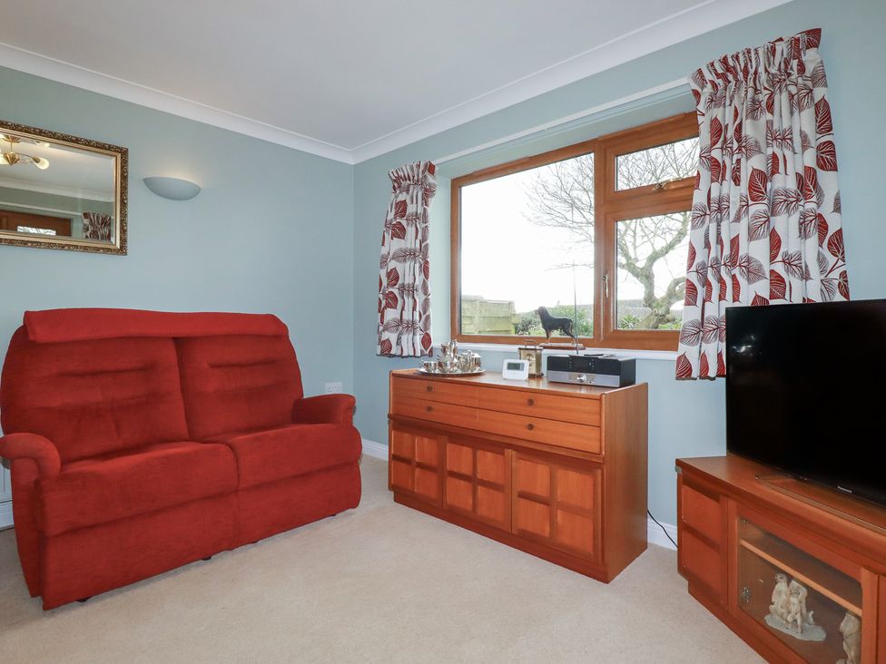 A living room with a red sofa and wooden furniture at Honeysuckle Rise in Looe