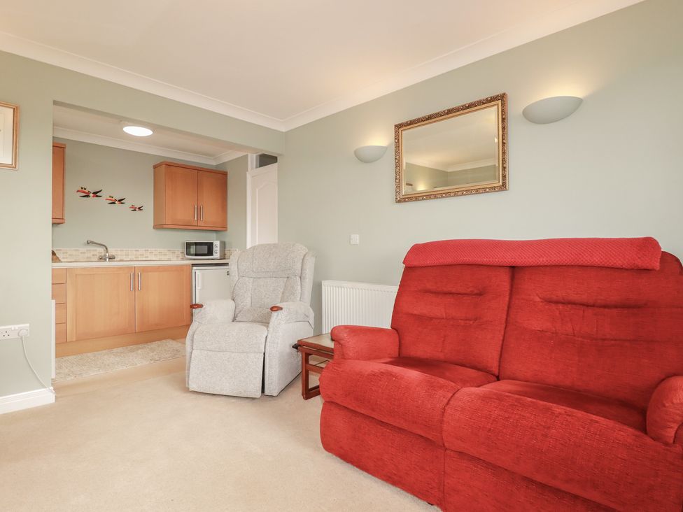 A living room with a red sofa and a recliner chair at Honeysuckle Rise in Looe