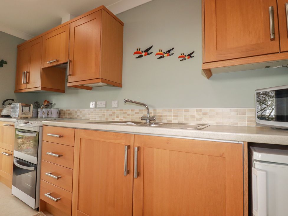 A kitchen with wooden cabinets and appliances at Honeysuckle Rise Looe