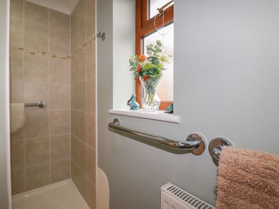 A bathroom with a shower and flowers on a windowsill at Honeysuckle Rise in Looe