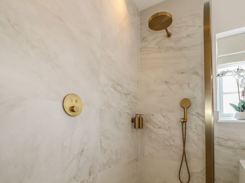 A shower with gold fixtures and marble wall tiles at Sea Estate House in Littlehampton