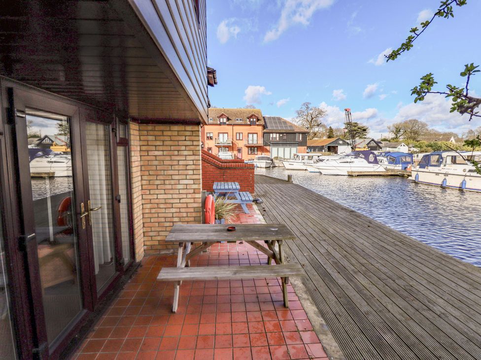 An outdoor area with a table and chairs overlooking a river at Grebe Cottage in Norwich