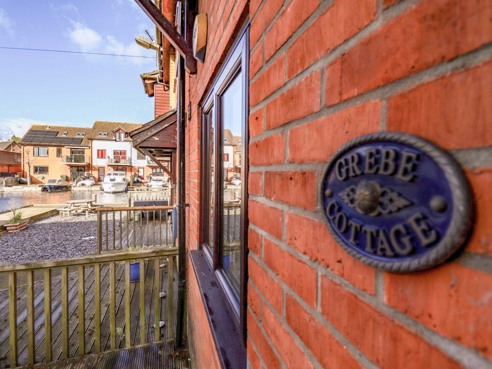 An outdoor view of Grebe Cottage with waterfront and boats in Norwich
