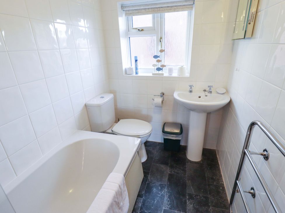 A bathroom with a bath tub, toilet, and sink at Grebe Cottage in Norwich