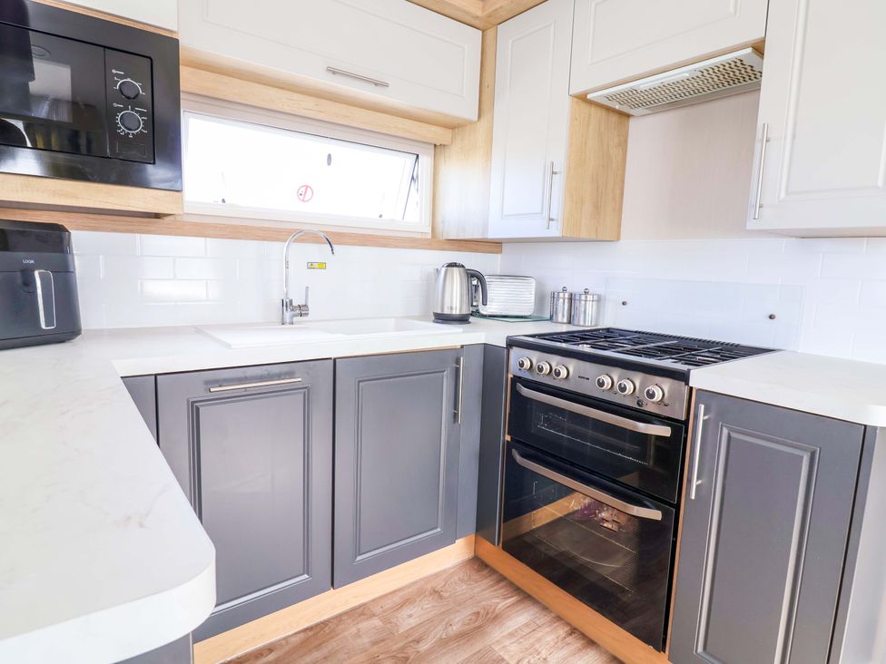 A kitchen with a stove, sink, and microwave at The Retreat Prestatyn