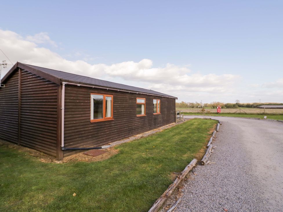 An outdoor view of a wooden lodge with grass and a gravel road at Lavender Lodge Evesham