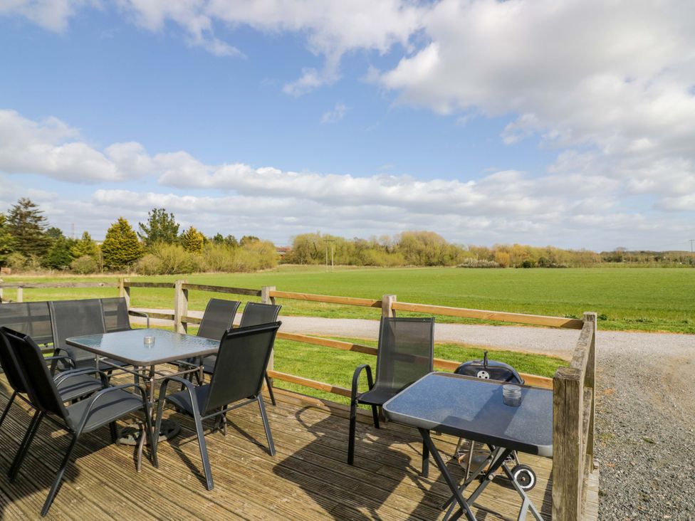 A deck with chairs and a table overlooking a field at Holly Lodge Evesham