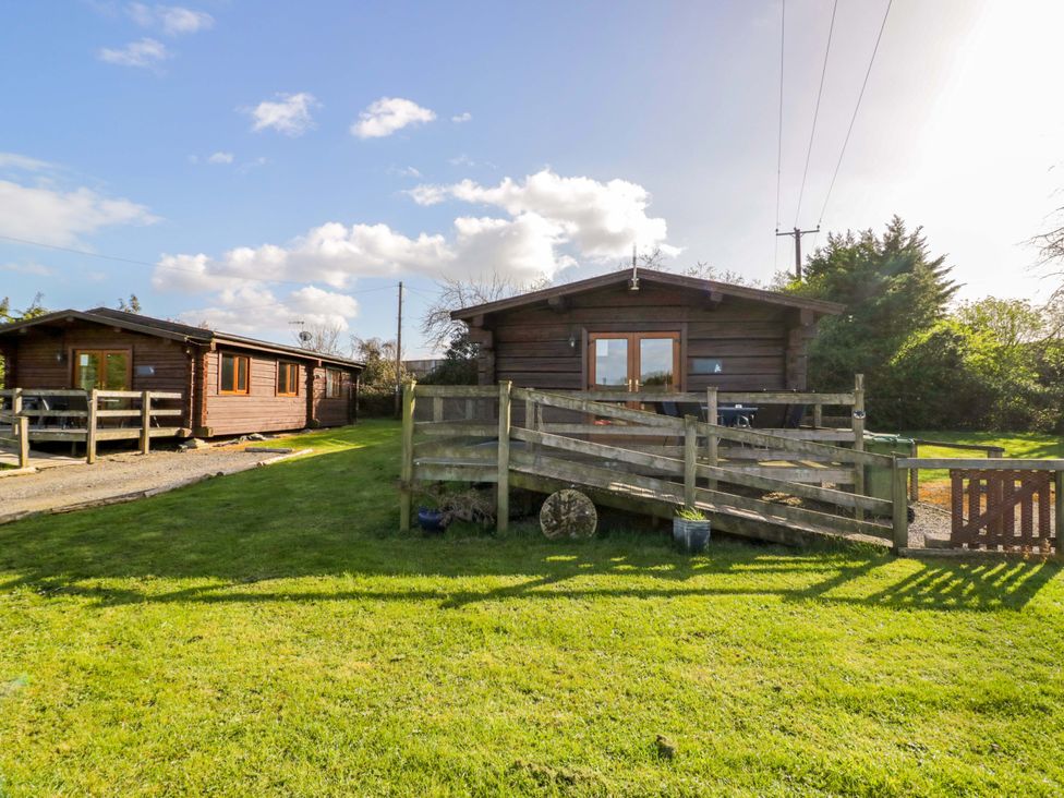 A wooden cabin with a fenced outdoor area at Primrose Lodge Offenham