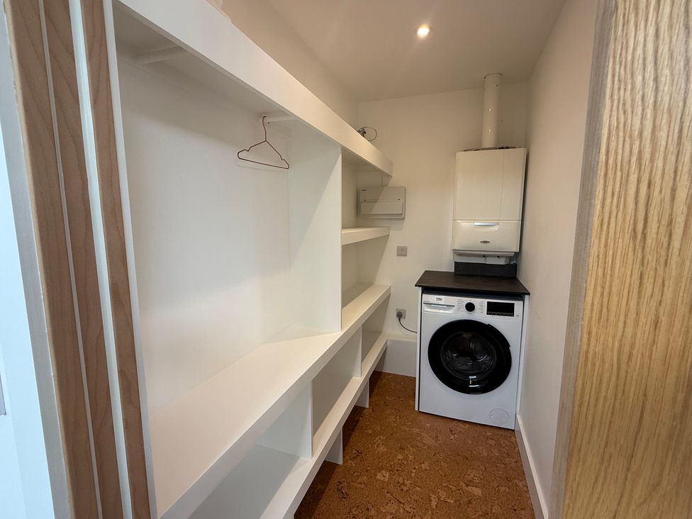 A utility room with a washing machine and shelves at Birdsong Gulval