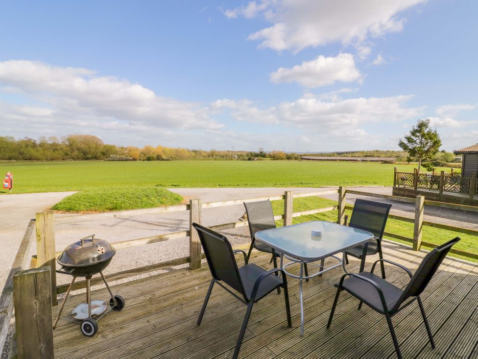 A table with chairs and a barbecue on a deck at Laurel Lodge Offenham