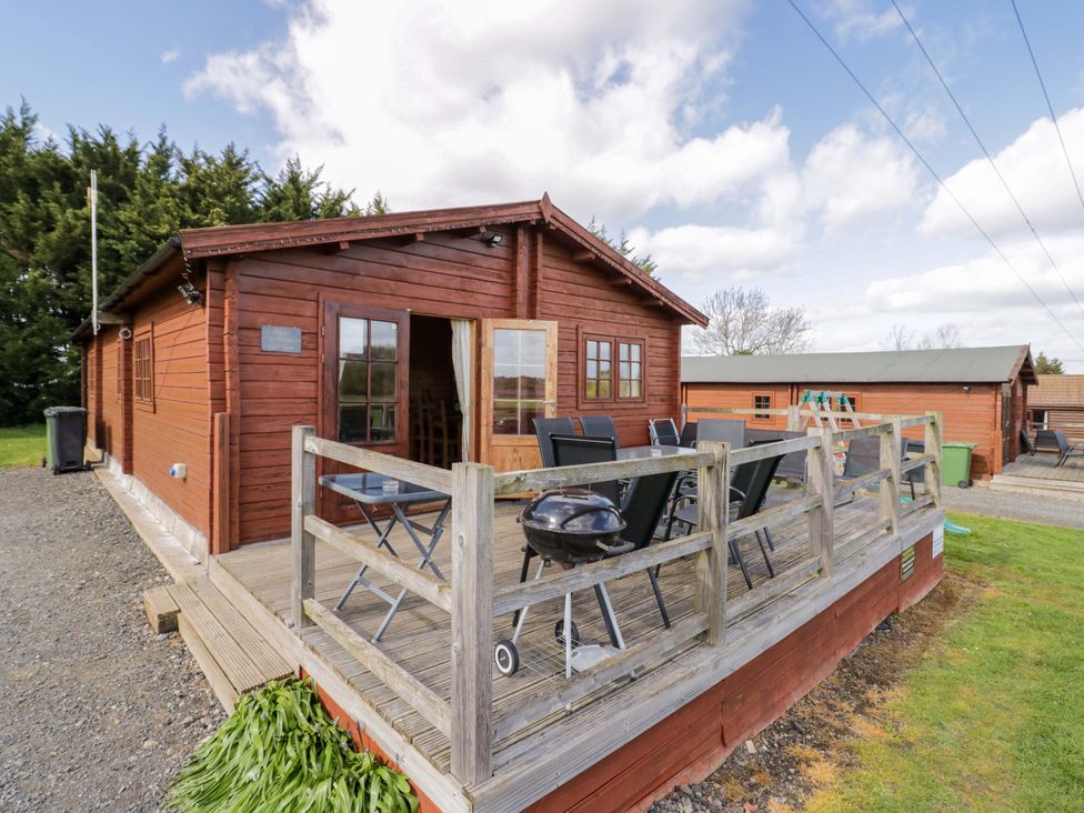 A wooden cabin with a deck and seating at Oak Lodge Offenham