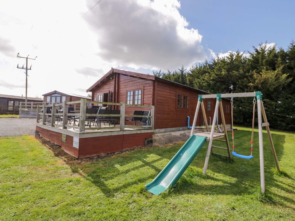 A cabin with a deck and swing set at Oak Lodge Offenham