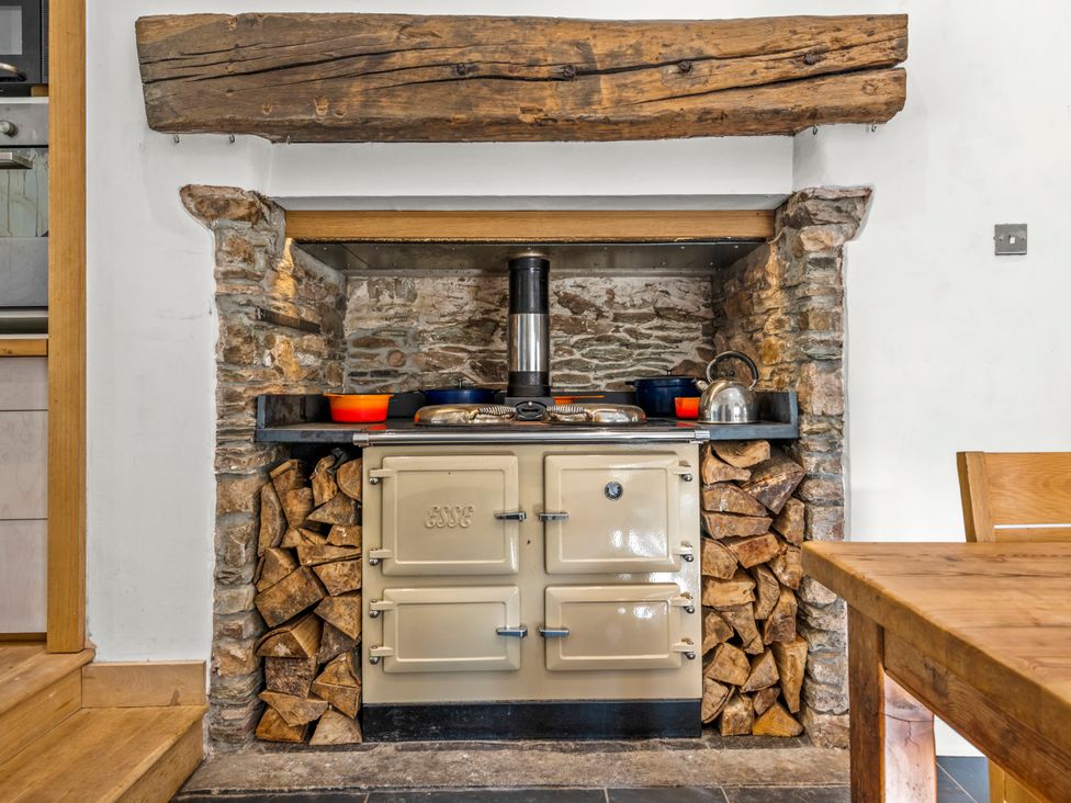 A kitchen with a stove and logs stacked in a stone wall at Chantry Studio in Kingsbridge