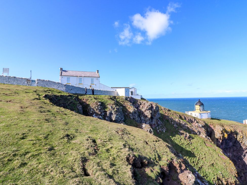 A cliffside view featuring a lighthouse and a house at The Lighthouse Bothy St Abbs