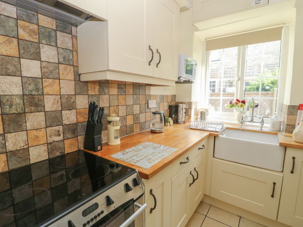 A kitchen with a stove, sink, and dish rack at Wedgewood Cottage in Middleham